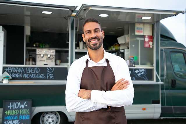 A young man in front of his food truck.