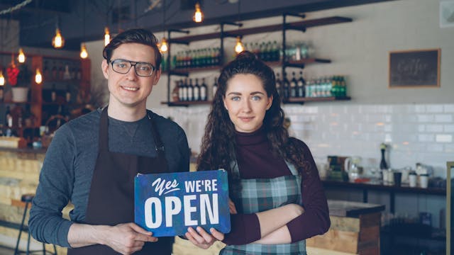 Pic of young married couple posing in their shop holding an open for business sign